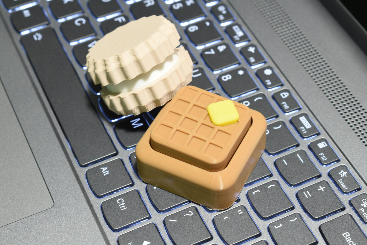 Layerplay CookieClick and WaffleClick 3D‑printed fidget clickers resting on a laptop keyboard.