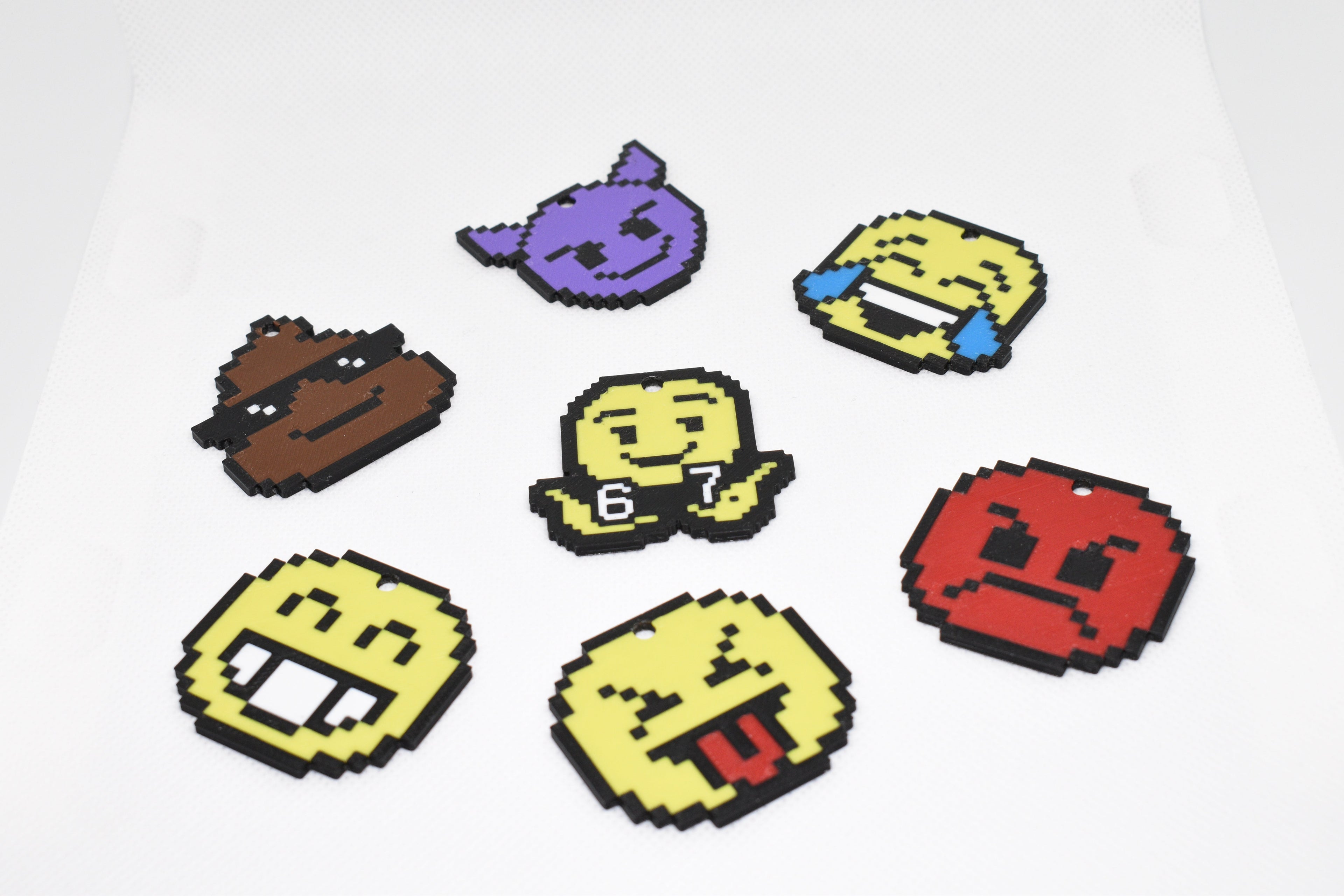 Seven pixel‑style emoji keychains with different expressions arranged on a white textured surface.