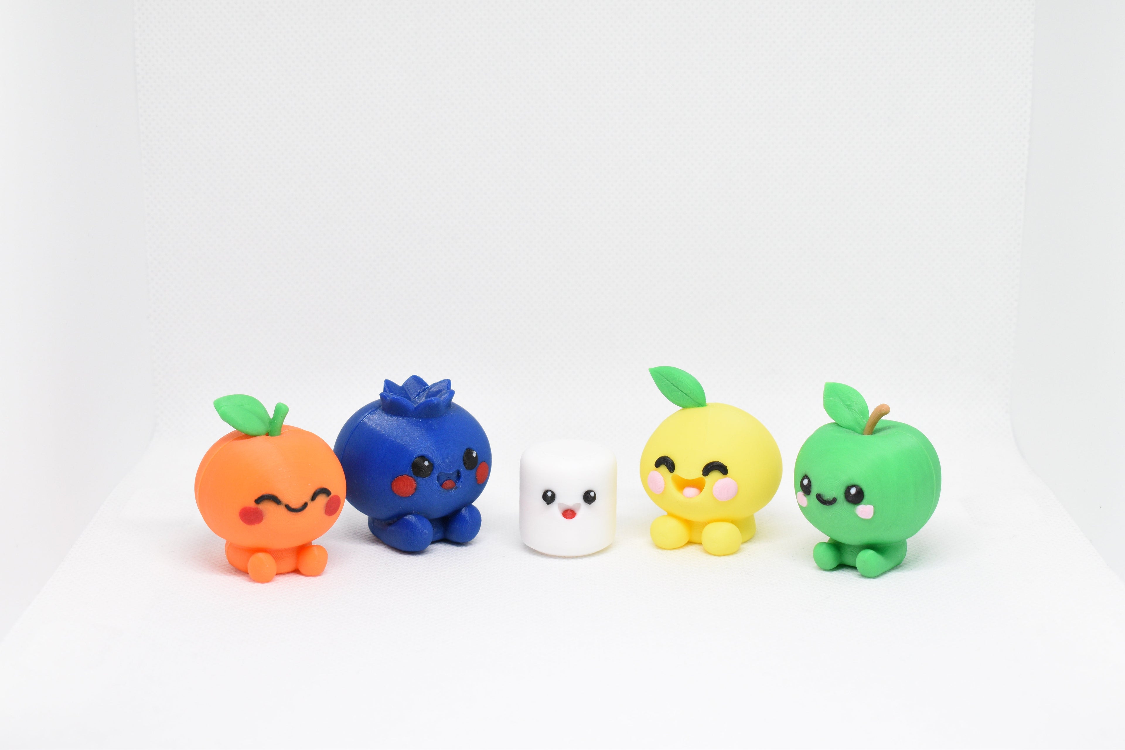Five colorful kawaii figurines arranged on a white textured surface.