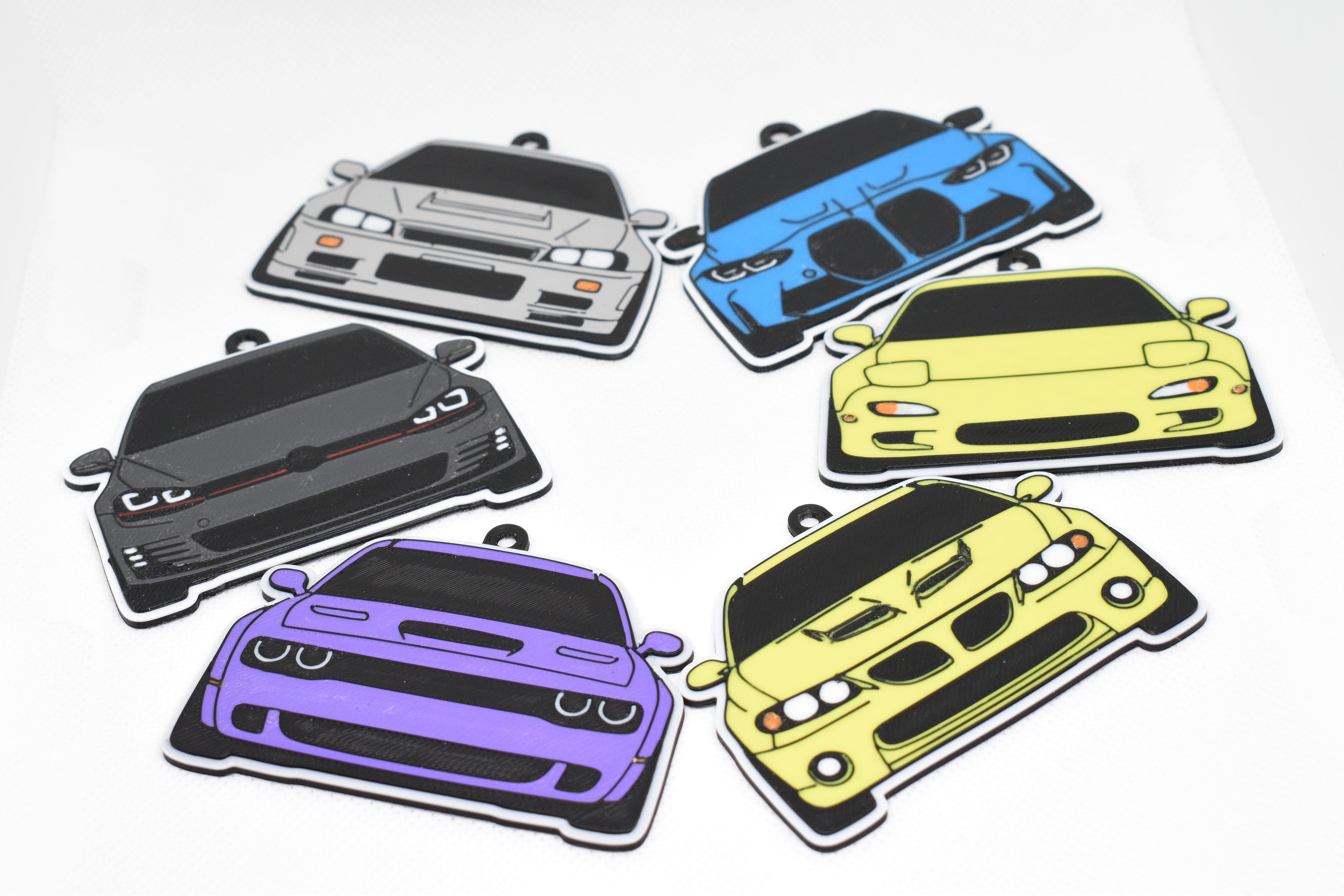 Six car keychain designs arranged on a white textured surface.