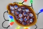 Overhead view of the Layertreat BulbBowl 3D printed candy dish filled with wrapped peppermint candies and framed by colorful glowing Christmas lights.