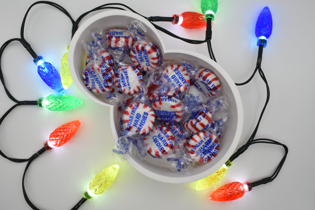 Overhead shot of the Layertreat FrostyBowl 3D printed snowman candy dish filled with wrapped peppermint candies, framed by colorful glowing holiday lights.