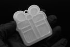 Handheld studio shot of a translucent 3D printed gift box present ornament featuring a ribbon bow detail on a black background.