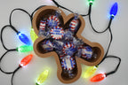 Overhead shot of the Layertreat GingerBowl 3D printed gingerbread man candy dish filled with wrapped peppermint candies and framed by colorful glowing holiday lights.