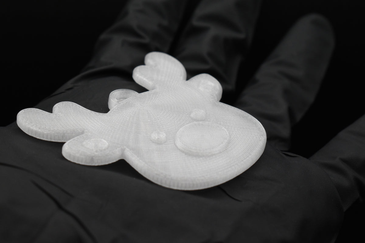 Close up of a 3D printed clear translucent reindeer Christmas ornament resting on a gloved hand against a dark backdrop.