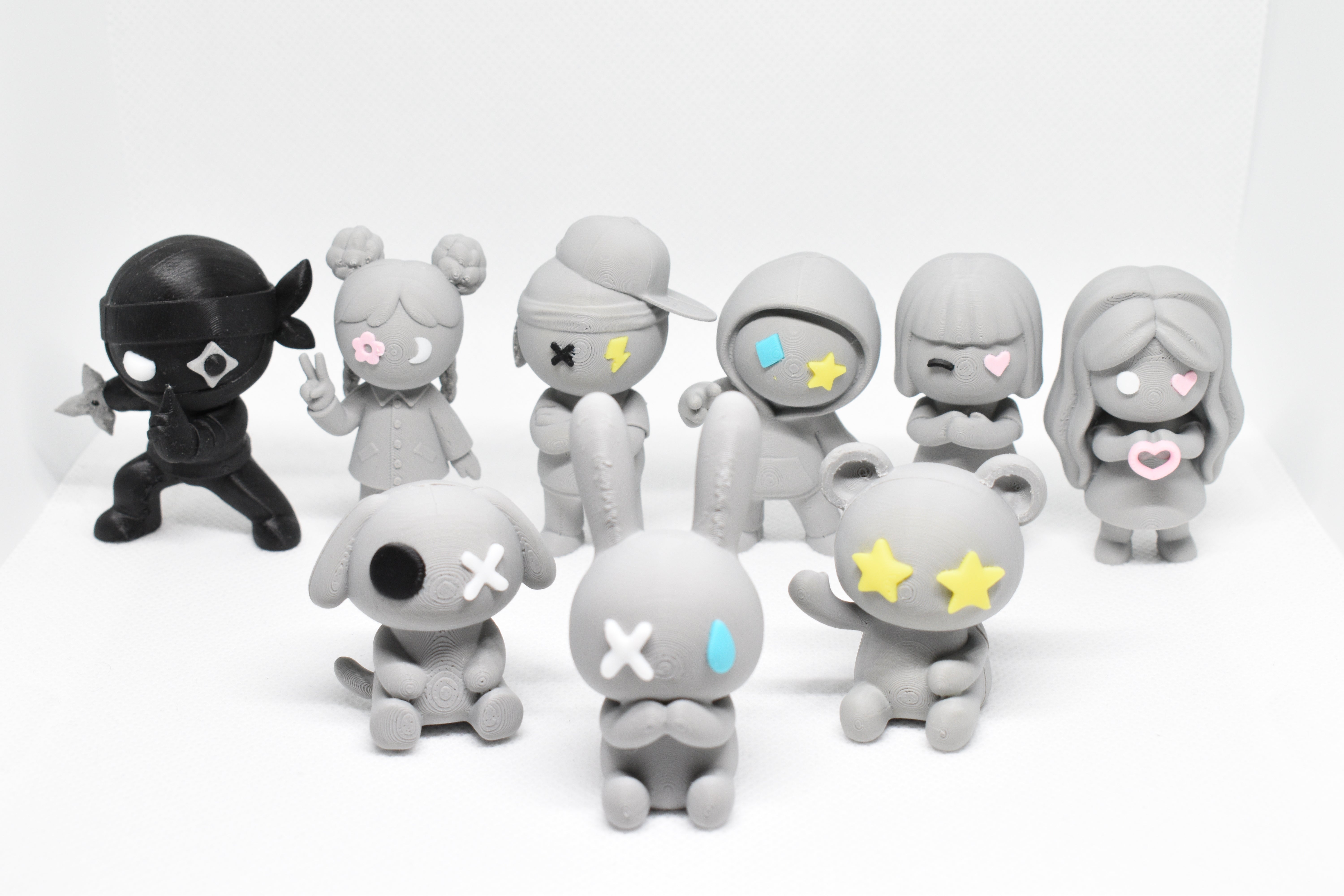 Group of nine Monomoodz figurines arranged on a white background, featuring characters with expressive symbol eyes.