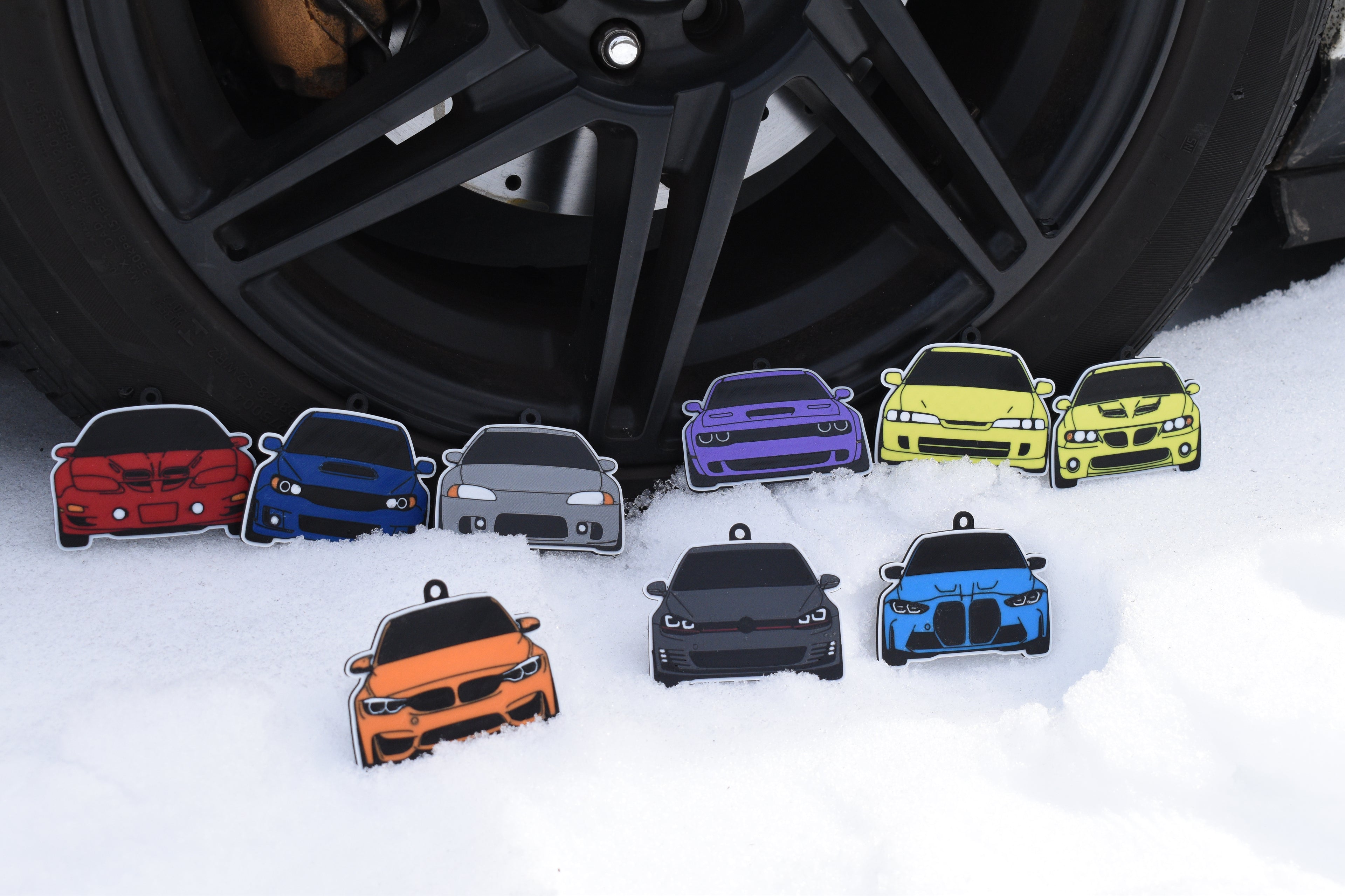 Pocket Motors collectible car pins lined up in front of a black car wheel on snowy ground.