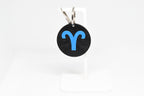 Aries zodiac keychain with blue symbol displayed on a white stand with metal ring and clip.
