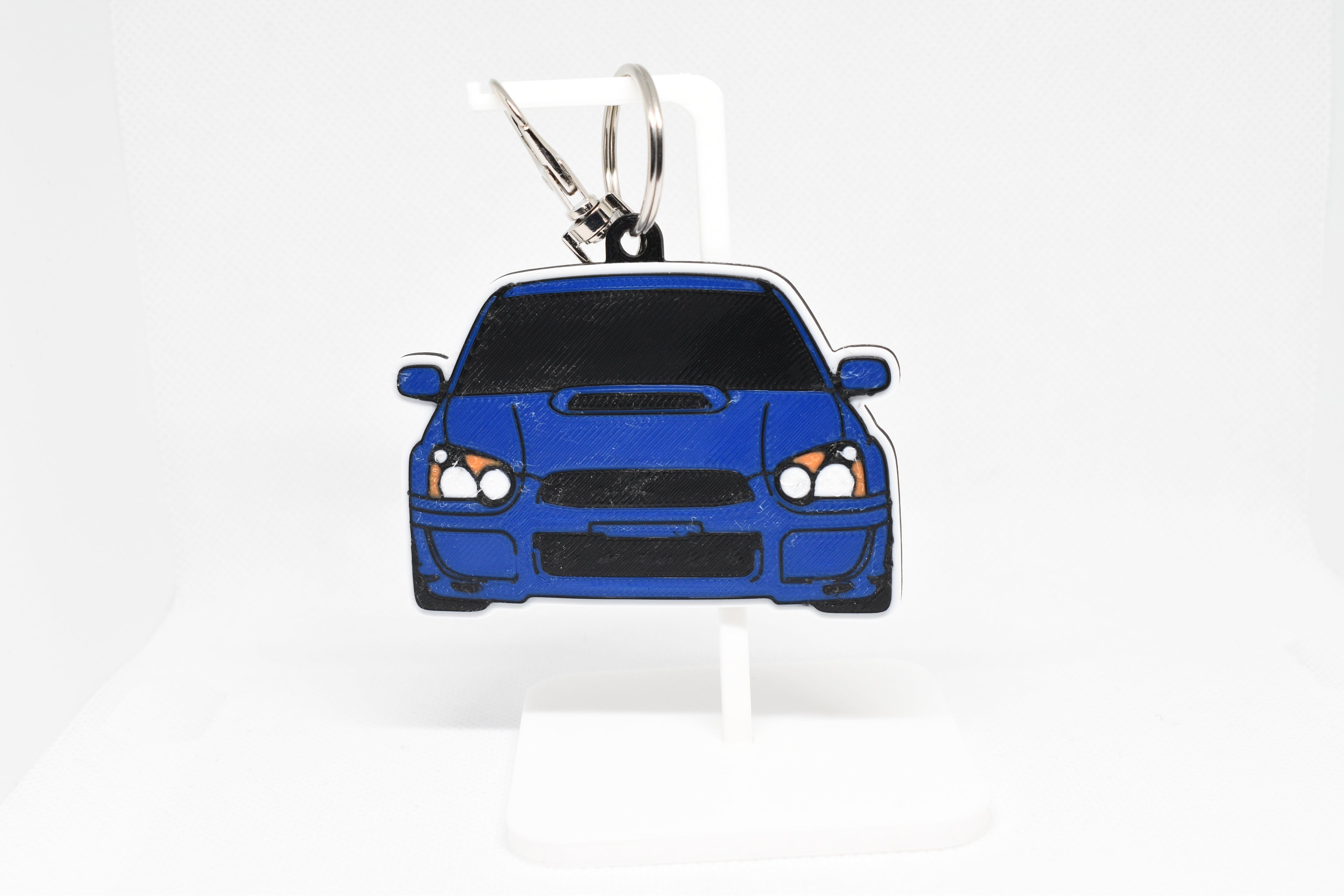 Blue Blobeye WRX STI keychain displayed on a white stand with metal ring and clip.