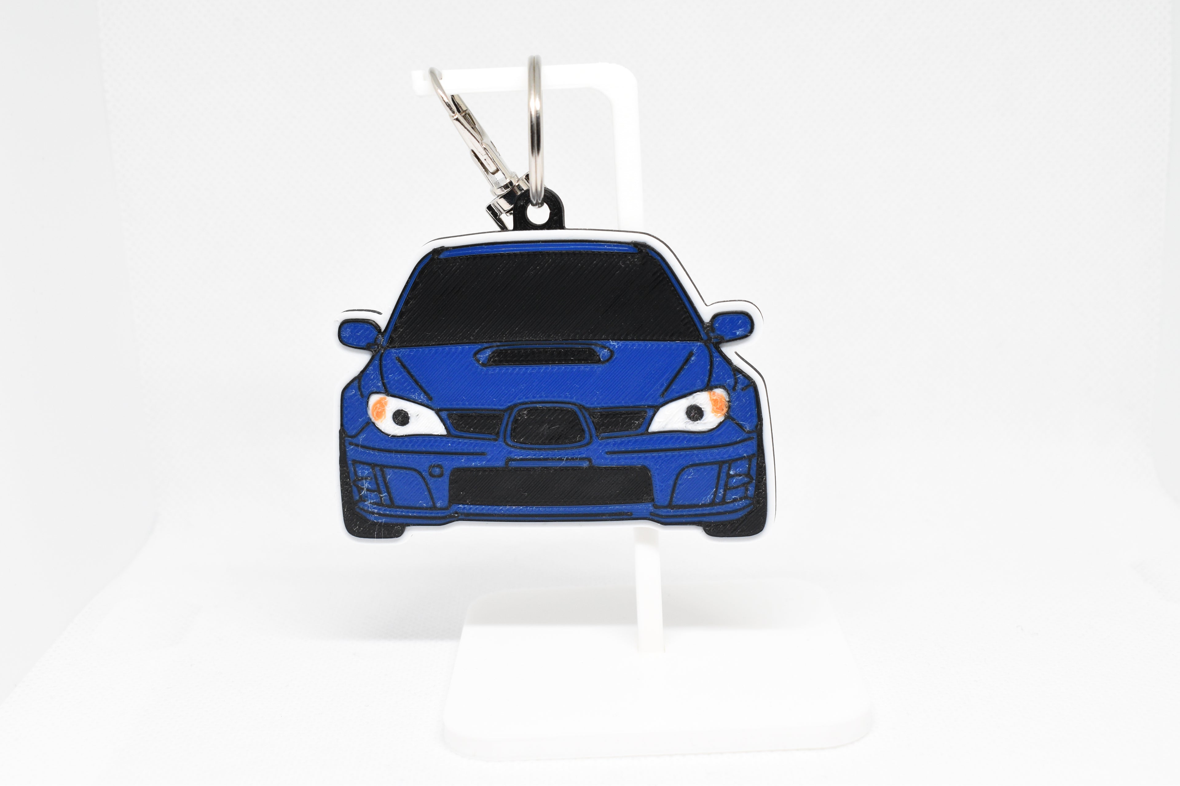 Blue WRX STI Hawkeye keychain displayed on a white stand with metal ring and clip.