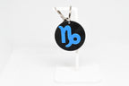 Capricorn zodiac keychain with blue symbol displayed on a white stand with metal ring and clip.
