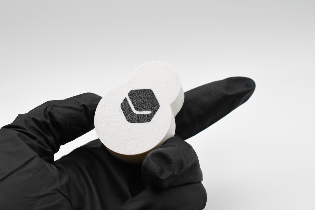 Gloved hand demonstrating the back base plate of the FrostyClick fidget toy, featuring a face-down textured plate finish and integrated Layerplay brand logo.