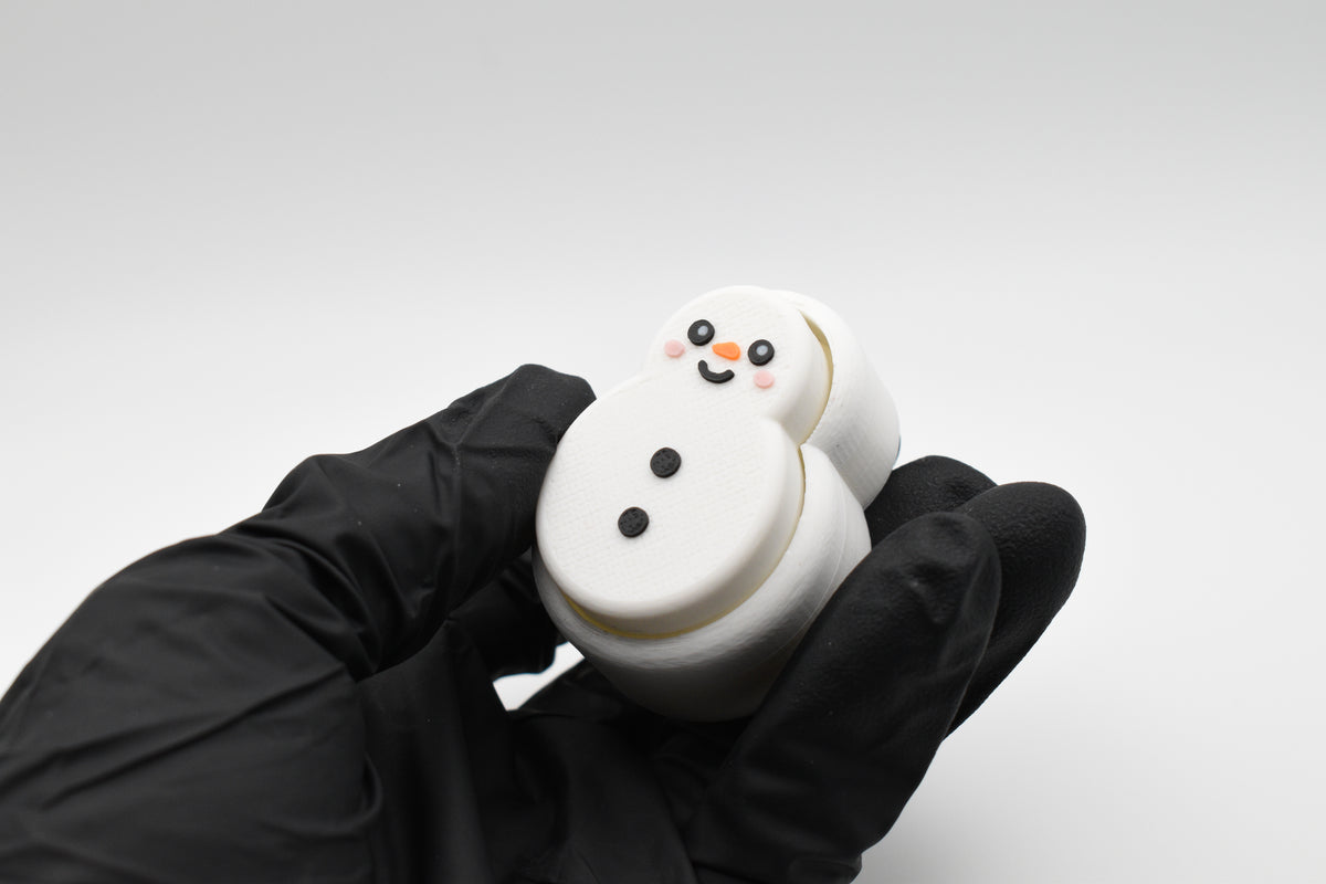 A gloved hand holding the FrostyClick snowman fidget clicker at an angle, highlighting its textured 3D printed body and mechanical switch button height.
