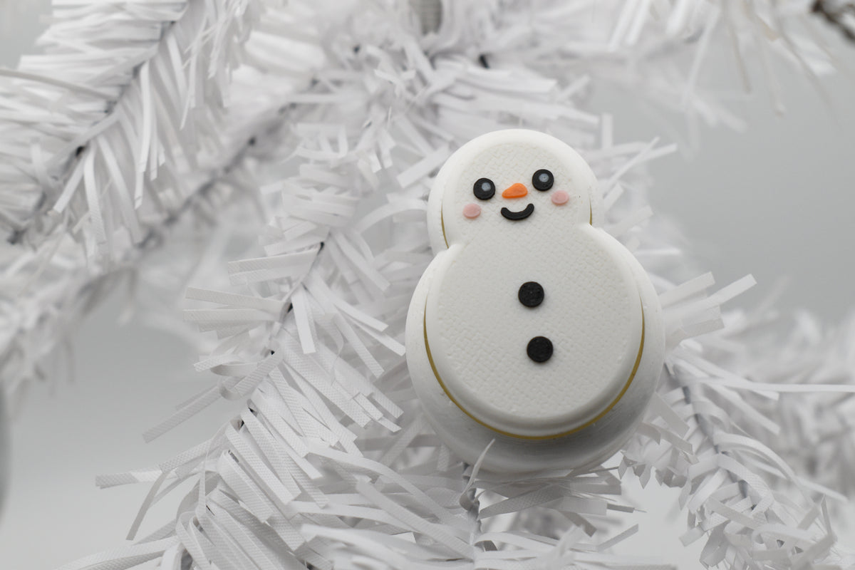 FrostyClick snowman mechanical keyboard switch fidget toy nestled in the branches of a white winter Christmas tree.