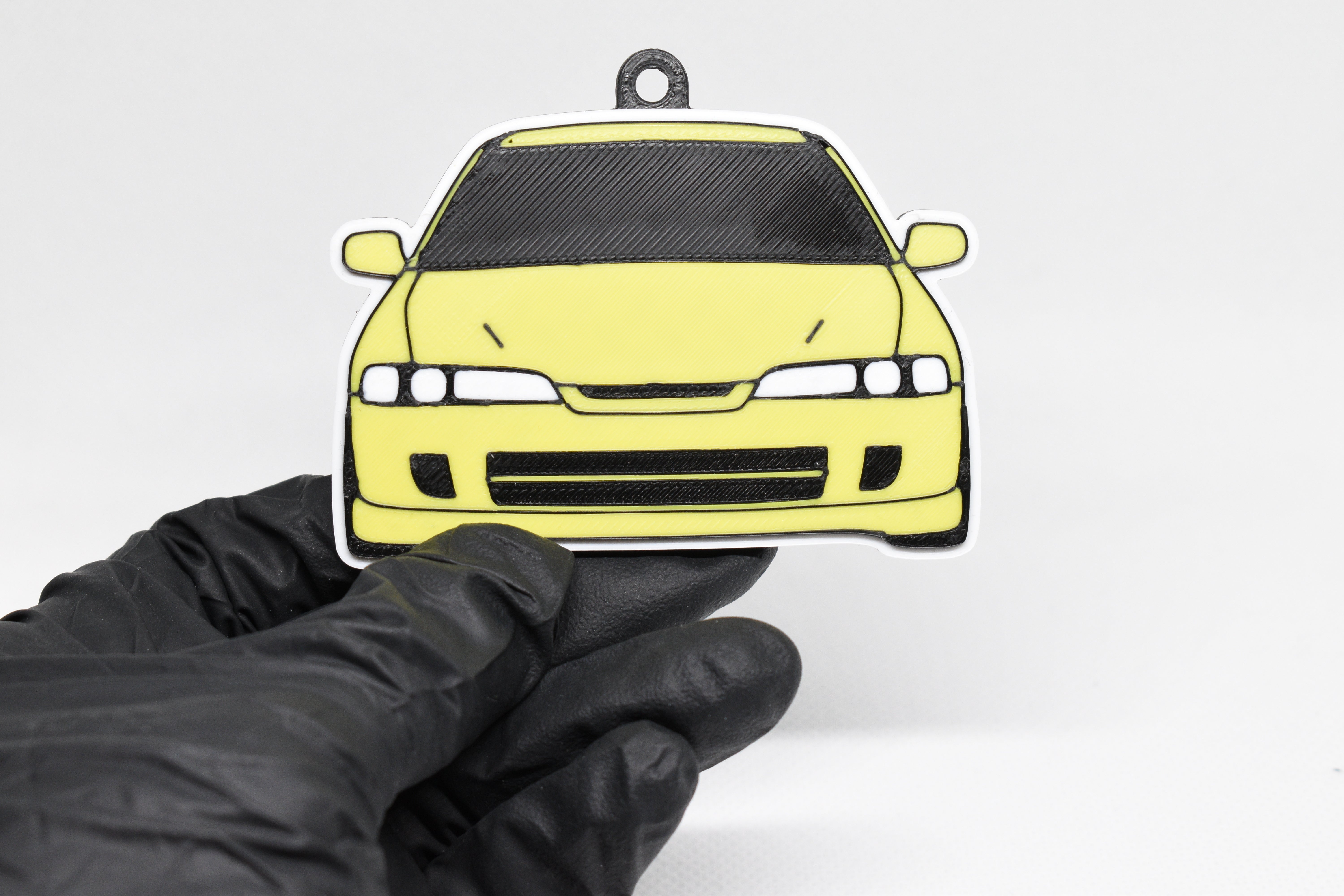 Yellow JDM Integra keychain held in a gloved hand against a white background.