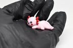 Hand in black glove holding cute 3D printed kawaii axolotl desk toy figure close up by LayerPlay