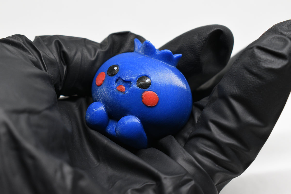 Hand in black glove holding cute 3D printed blue kawaii blueberry desk toy figurine close up by LayerPlay