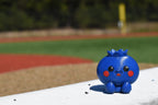Cute 3D printed blue kawaii blueberry desk toy sitting outdoors on a white ledge with a sports field background by LayerPlay