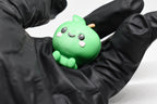 Hand in black glove holding cute 3D printed green kawaii green apple desk toy figurine close up by LayerPlay