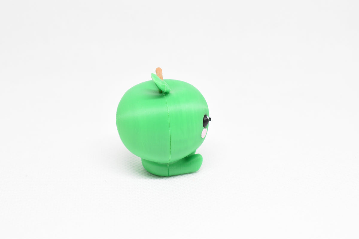Side profile view showing round green body and leaf stem detail of 3D printed kawaii green apple desk toy by LayerPlay