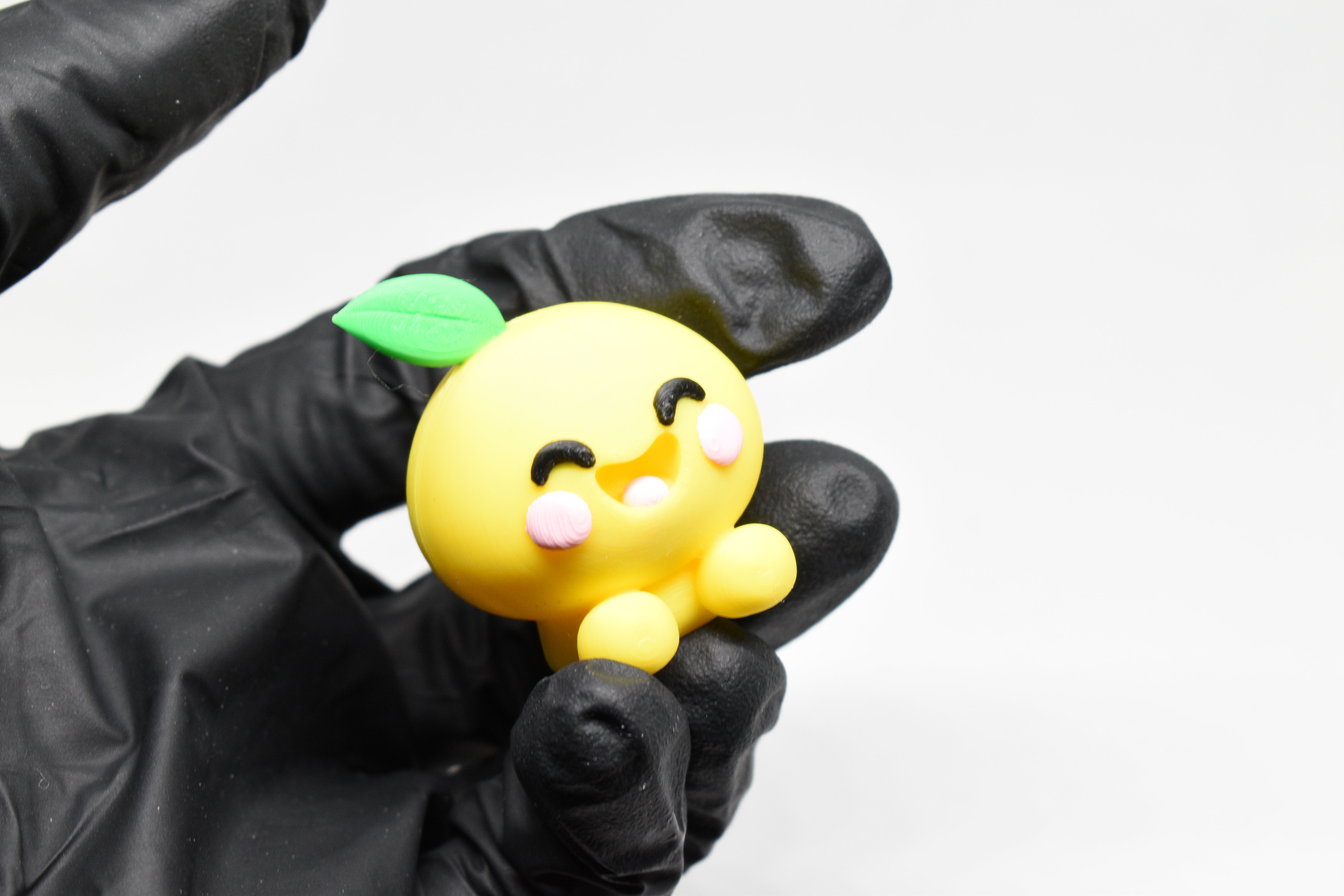 Kawaii Lemon figurine with green leaf held in gloved fingers against a white background.