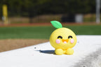Cute 3D printed yellow kawaii lemon desk toy sitting outdoors on a white ledge with a green sports field background by LayerPlay