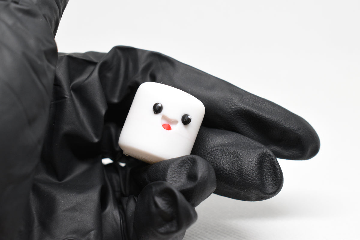 Hand in black glove holding cute 3D printed white kawaii marshmallow desk toy figurine close up by LayerPlay