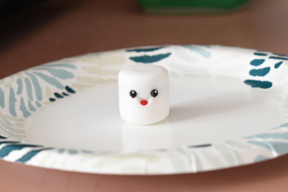 3D printed kawaii marshmallow desk toy figurine sitting on a patterned paper plate display setting by LayerPlay