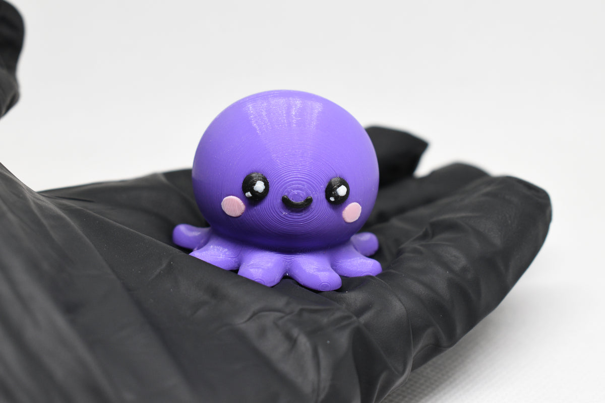 Hand in black glove holding cute 3D printed kawaii octopus desk toy figure close up by LayerPlay