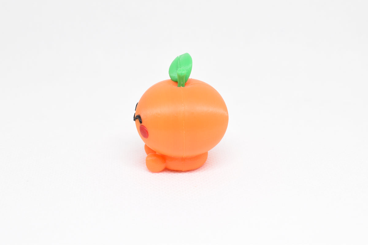 Side profile view showing round orange body and green leaf detail of 3D printed kawaii orange desk toy by LayerPlay
