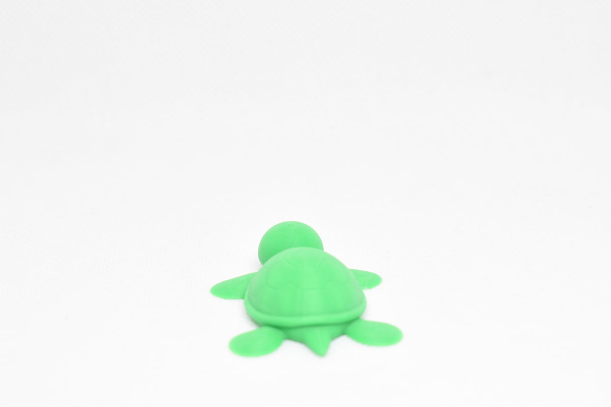 Low angle view of cute 3D printed kawaii sea turtle desk toy figure resting on a white background by LayerPlay
