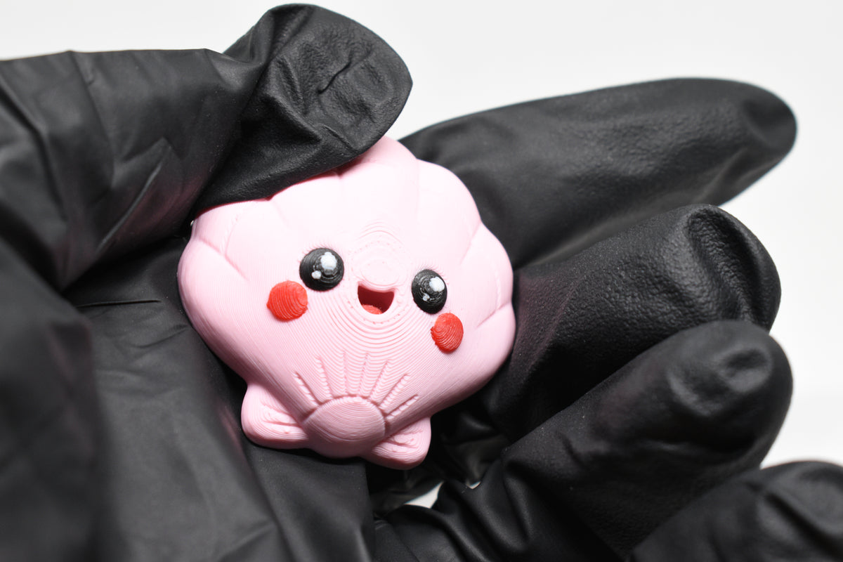 Hand in black glove holding cute 3D printed kawaii seashell desk toy figure close up by LayerPlay