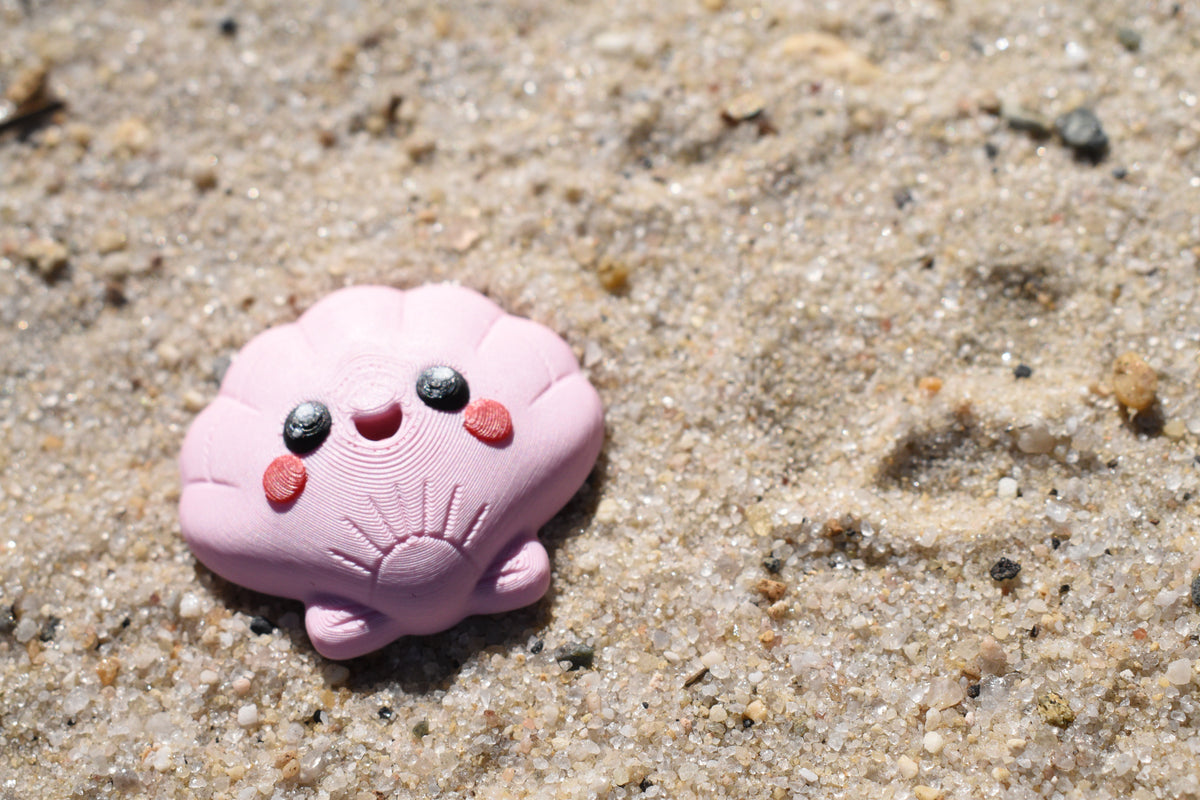 3D printed kawaii seashell desk toy figurine resting outdoors on beach sand by LayerPlay