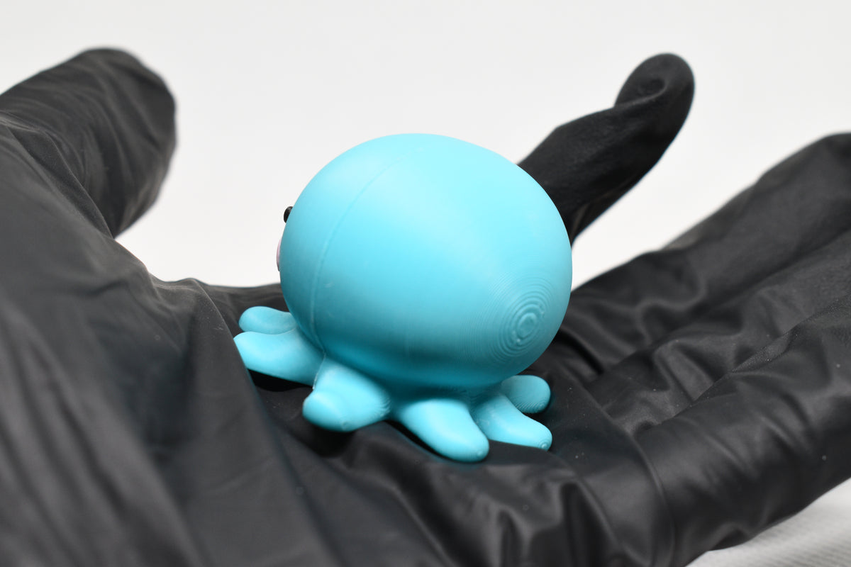 Hand in black glove holding cute 3D printed kawaii sleeping octopus desk toy figure close up by LayerPlay