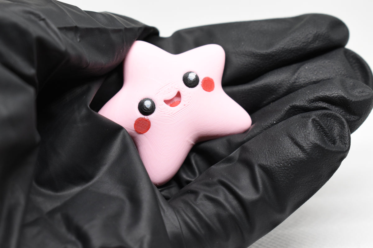 Hand in black glove holding cute 3D printed pink kawaii starfish desk toy figure close up by LayerPlay