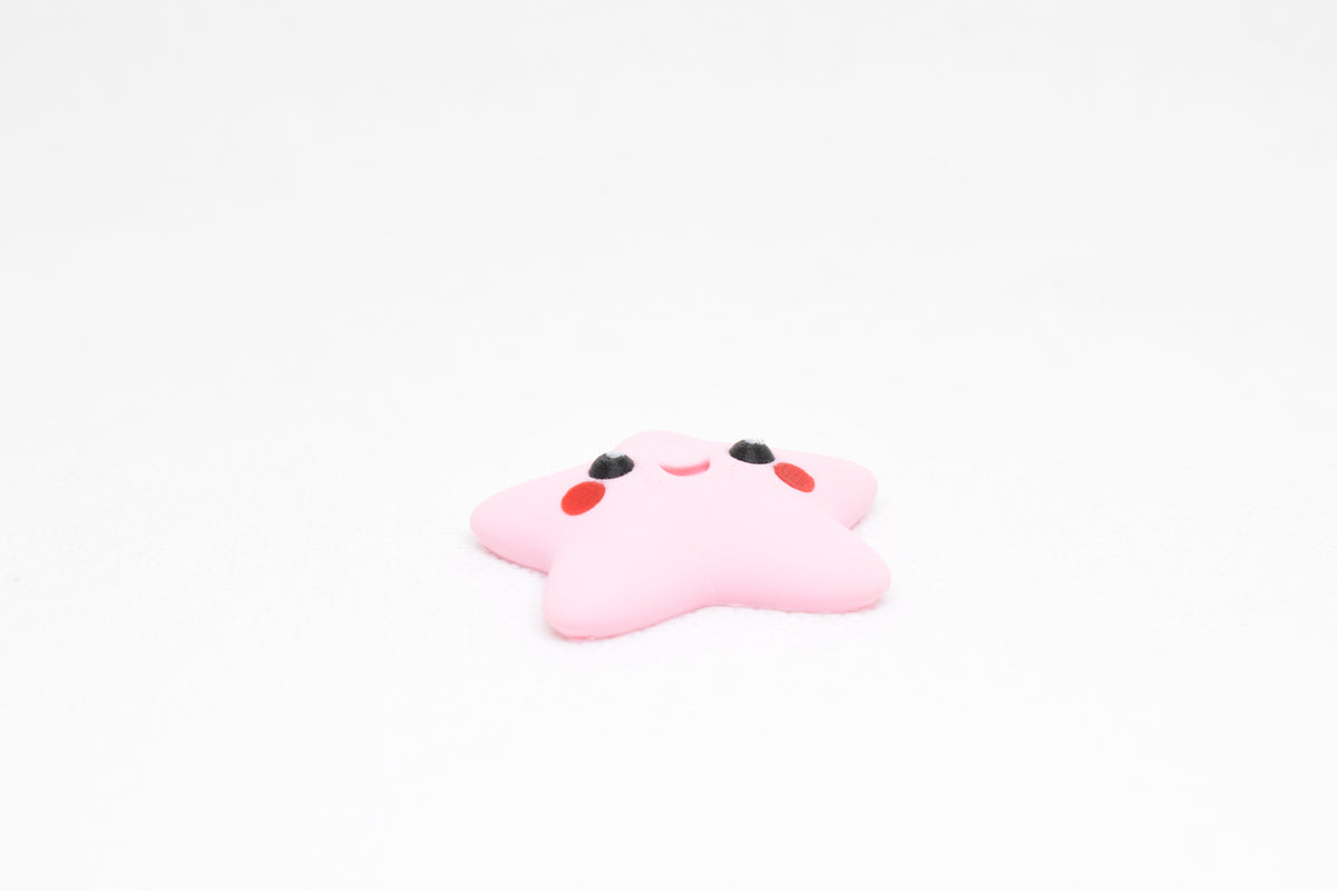 Low angle view of cute 3D printed pink kawaii starfish desk toy figure resting on a white background by LayerPlay