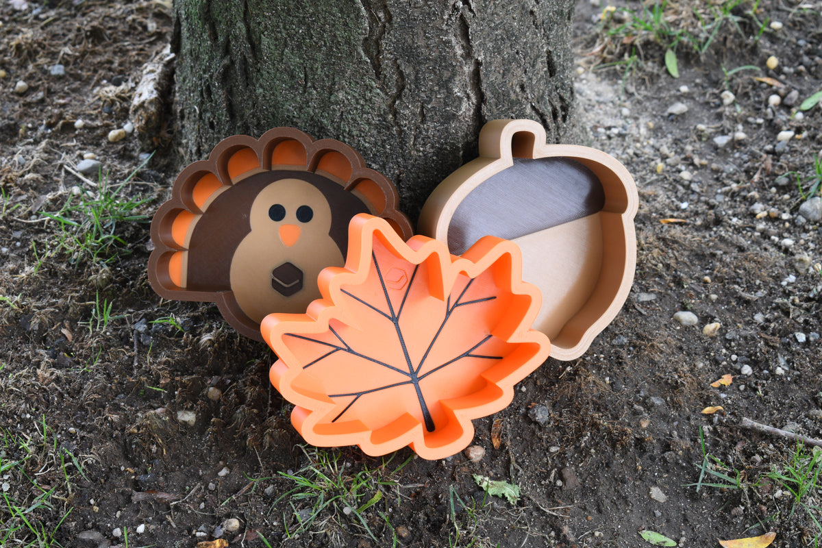 Layertreat Fall Series candy dishes — MapleBowl, AcornBowl, and GobbleBowl — displayed outdoors at the base of a tree.