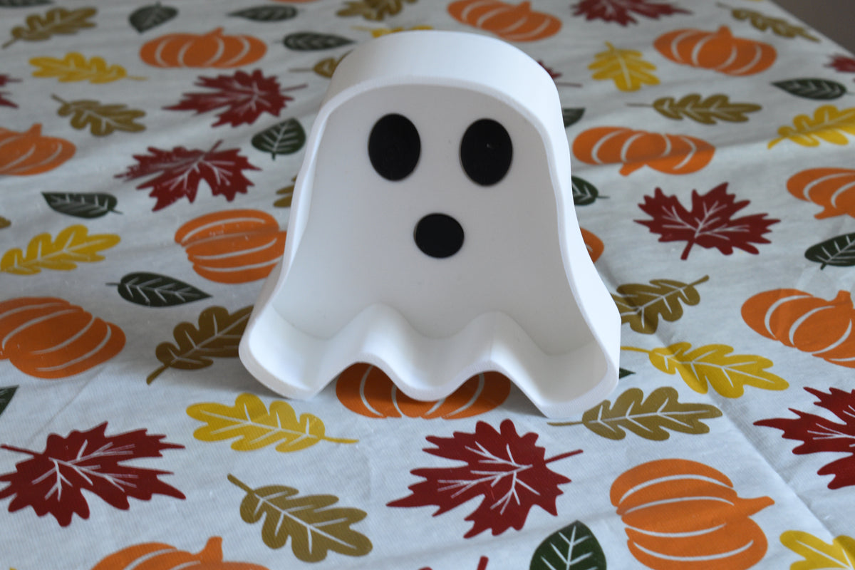 3D printed white ghost candy dish displayed upright on a fall patterned tablecloth with leaf and pumpkin print by LayerPlay Layertreat