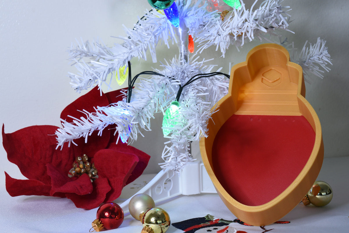 Layertreat BulbBowl red and gold Christmas light bulb 3D printed candy dish set up in a holiday tree display with red poinsettia and ornaments.