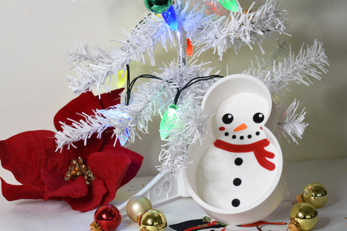 Layertreat FrostyBowl 3D printed white snowman candy dish displayed upright under a lit white Christmas tree with red poinsettia flower and ornament accents.