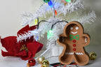 Layertreat GingerBowl 3D printed gingerbread man candy dish styled under a lit white Christmas tree next to a red poinsettia flower and metallic ornaments.