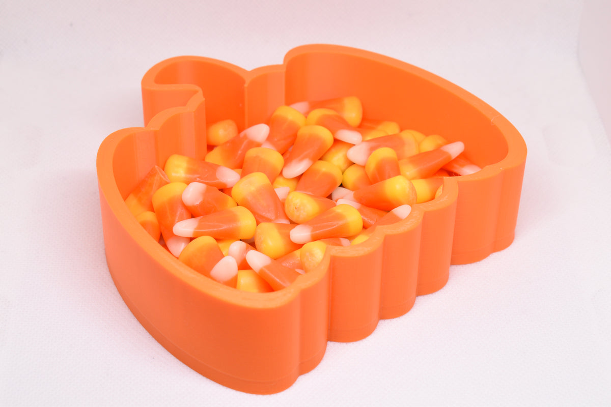 Angled studio view of 3D printed orange jack-o'-lantern candy dish filled with candy corn for Halloween decor by LayerPlay Layertreat
