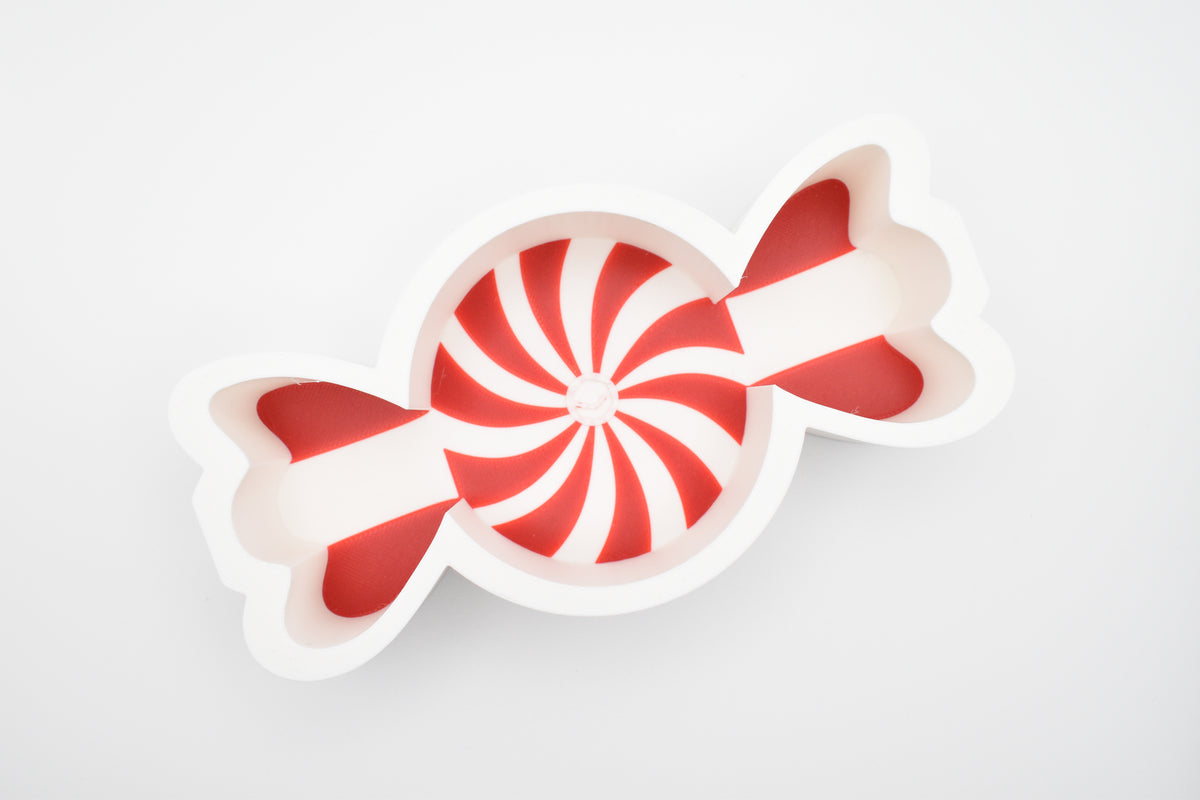 Top-down view of the Layertreat 3D printed peppermint candy dish shaped like a wrapped candy with red and white swirl accents on a clean white background.