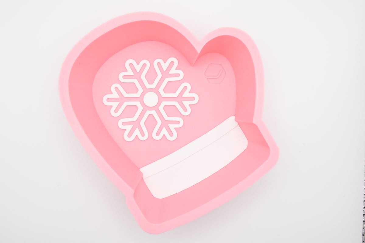 Top-down view of the Layertreat MittenBowl, a pastel pink 3D printed winter mitten candy dish featuring a white snowflake design and white cuff accent on a clean white background.
