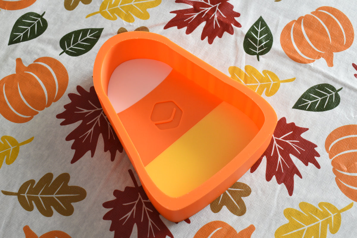 3D printed tri-color candy corn dish displayed on a fall patterned tablecloth with leaf and pumpkin print by LayerPlay Layertreat