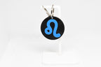 Leo zodiac keychain with blue symbol displayed on a white stand with metal ring and clip.