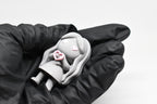 Hand in black glove holding cute grey 3D printed monomoodz corra heart desk figure close up by LayerPlay