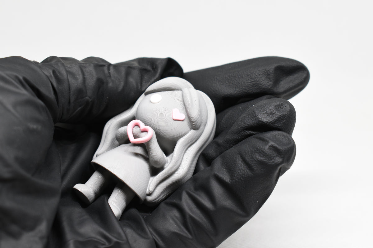 Hand in black glove holding cute grey 3D printed monomoodz corra heart desk figure close up by LayerPlay
