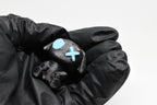 Hand in black glove holding 3D printed black monomoodz glow in the dark glyphie dog figure with white X and glow circle eyes close up by LayerPlay