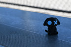 3D printed black monomoodz glow in the dark glyphie dog figure sitting outdoors on metal stadium bleachers by LayerPlay
